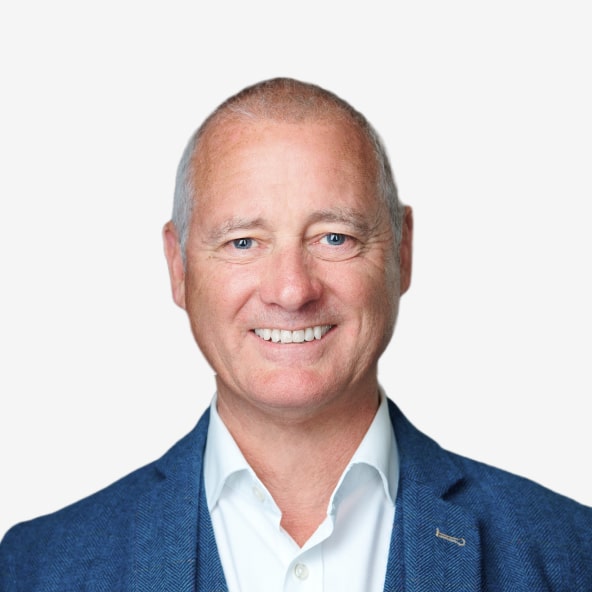 Smiling middle-aged man with short gray hair, wearing a blue blazer over a white shirt, standing against a plain white background.