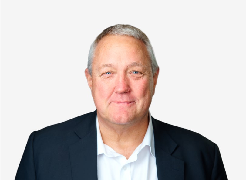 A middle-aged man with short gray hair wearing a dark suit jacket and white shirt, smiling, against a plain white background.